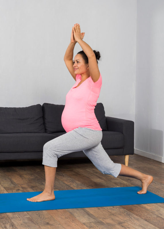 side view of pregnant woman at home with exercising mat practicing yoga position